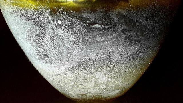 Ice condensing on a  yellow glass tumbler with ice frozen into the bottom, and subzero Jägermeißter foating on top of the water ice sea floor, resembles an ice moon.