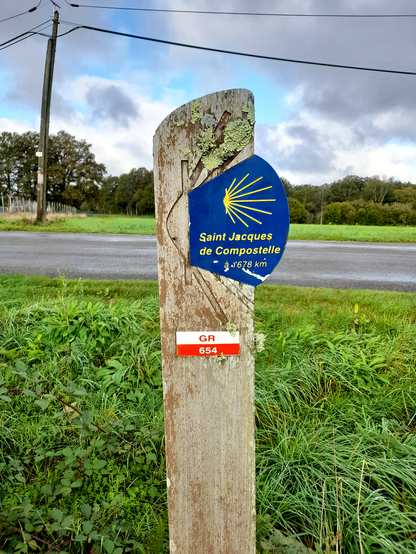 A blue sign with the St James symbol that says it is 1678 kilometers to Santiago de Compostela.