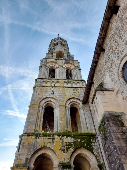 Looking up at a church tower against a blue sky. A lot of moss is growing on the lower part of the tower.