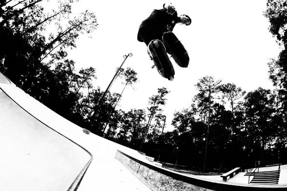A black and white photo showing a low angle view of an inline skater high above a bowl at an urban skatepark.