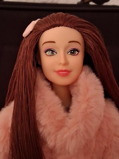 La muñeca de cerca. El cabello lo tiene hecho con hilo castaño y llega un pasador de color rosita y con forma de corazón. La cara tiene una expresión dulce e inocente