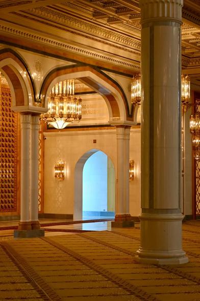 View from inside of a big, modern (but ornate) mosque. Most of the picture is bathed in yellow and orange tones, but blue light shines in through a doorway.