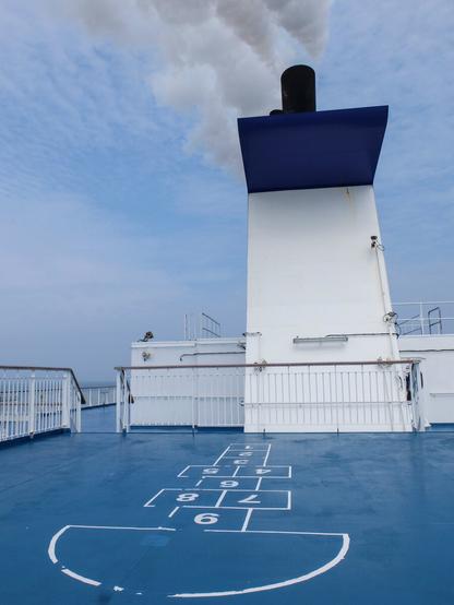 A hopscotch is being drawn on the deck of a ferry. In the background, smoke is billowing from the ship's huge chimney.