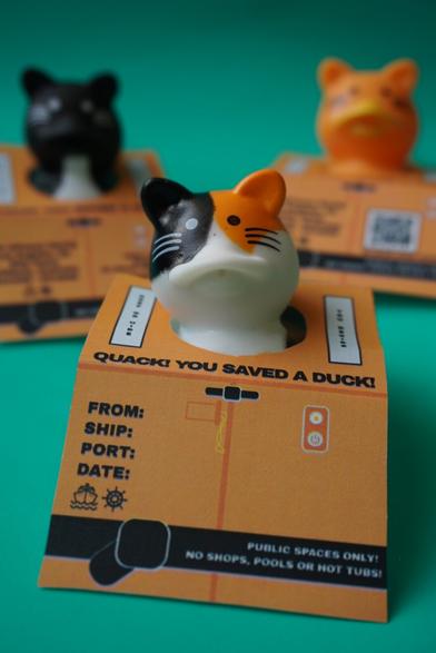 Cat shaped rubber ducks with tags around their necks. Tags are made for hiding ducks on a cruise and are styled as little life jackets.