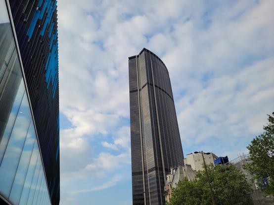 Tour Montparnasse dans un ciel bleu parsemé de nuages blancs. Bâtiment vitré dans lequel se reflète le ciel