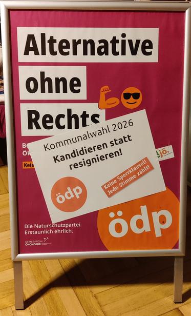 Das Bild zeigt ein Wahlplakat der Ökologisch-Demokratischen Partei (ödp) in einem silbernen Aufsteller mit einem auffälligen pinken Hintergrund. Der zentrale Slogan lautet:

„Alternative ohne Rechts“

Darüber geklebt ist ein zusätzliches weißes Schild mit dem Aufdruck:

„Kommunalwahl 2026 – Kandidieren statt resignieren!“
Dazu das ÖDP-Logo und der Hinweis: „Keine Sperrklausel! Jede Stimme zählt!“