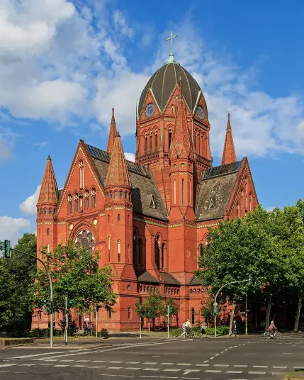 The image features a large, ornate brick building with a distinct architectural style, displaying pointed towers and a domed roof with a cross. The building is surrounded by trees and is situated at a street intersection. The sky is partly cloudy, suggesting a clear day. This type of structure is often associated with churches or similar religious edifices.

Image Credits: Wikimedia / A.Savin / CC BY-SA 3.0
