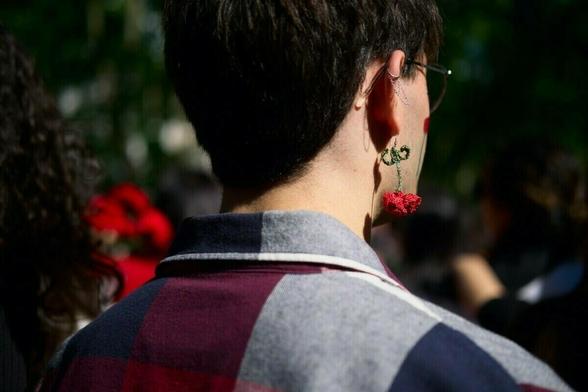 A person wearing glasses has a large, red flower earring, viewed from behind.