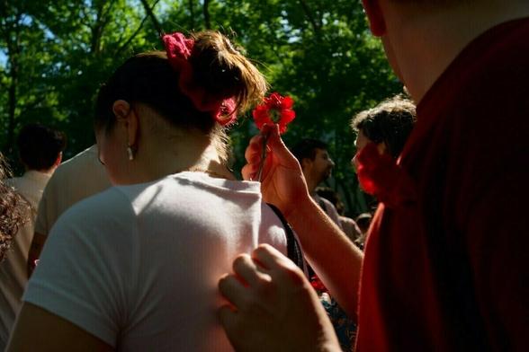 A group of people outdoors, with one person holding a red flower and another wearing a red flower hair accessory.