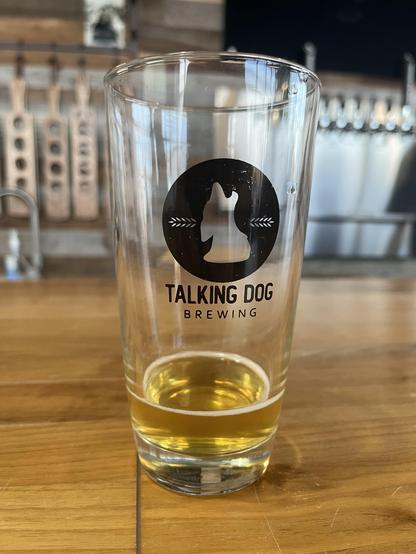 An almost empty glass of golden beer with a howling dog logo on the glass and the words Talking Dog Brewing.