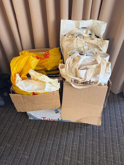 Three boxes sitting on a hotel room floor, filled with canvas and plastic bags, themselves filled with old convention stuff.