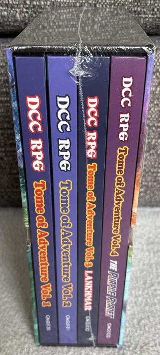 The slipcase set shown from the side, containing thick hardcover books of compiled DCC RPG adventures.