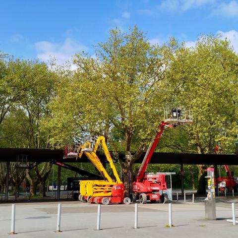 Foto der Teleskop - Arbeitsbühnen auf einem Parkplatz vor frühlingsgrünen Bäumen.