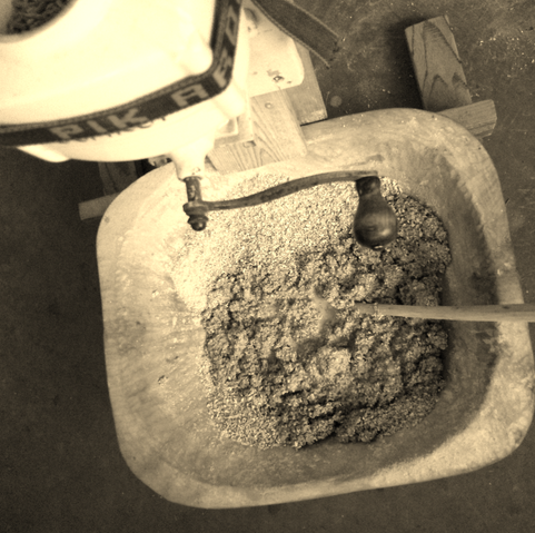 Das Bild zeigt eine Holzmolle mit Sauerteig und frisch eingemahlenem Roggenschrot. Die Schrotmühle mit Handkurbel ist auch zu sehen