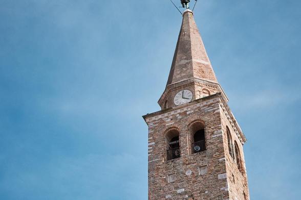 Brick church tower with a clock face and pointed spire against a clear blue sky.