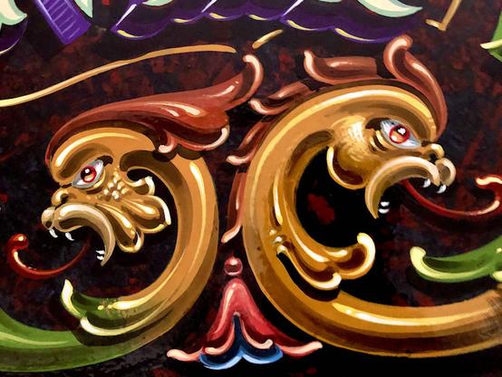 Two fierce-looking dragon heads, back to back, painted in the ornate Fileteado Porteño style.