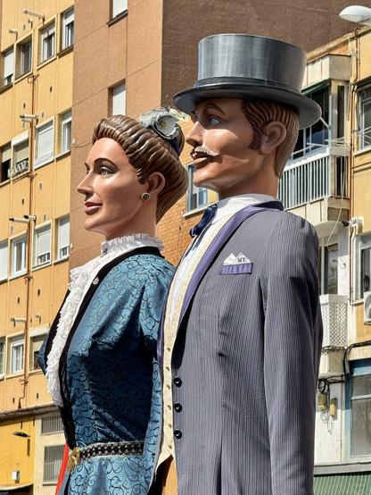Detalle de los cabezudos. Señor con traje y sombrero en primer plano y señora también de punta en blanco a su lado.