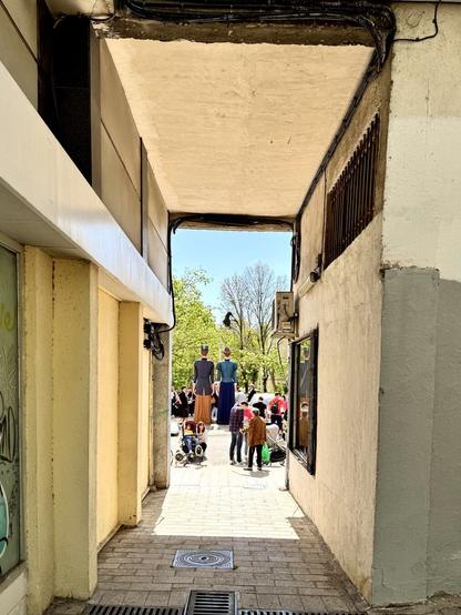 Vista de los dos cabezudos desde el pasaje que da a la plaza donde están. Se les ve de espaldas sobresaliendo sobre la multitud.