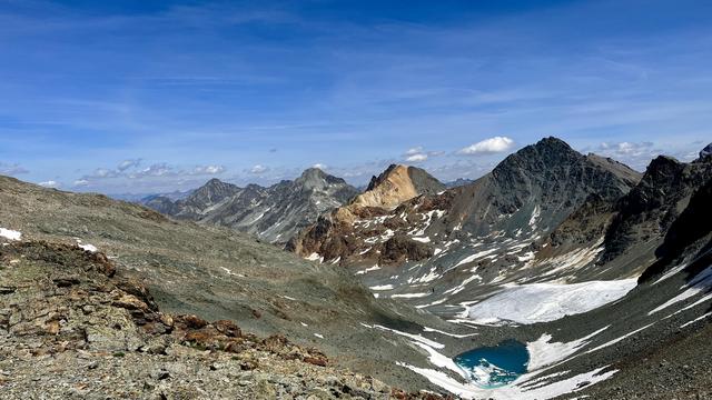 Foto einer kargen Berglandschaft, aufgenommen von der Fuorcla da Flix. In der Bildmitte ist der Piz Traunter Ovas zu sehen, der aufgrund seiner Gesteine links gelb-orange und rechts dunkelgrau ist.