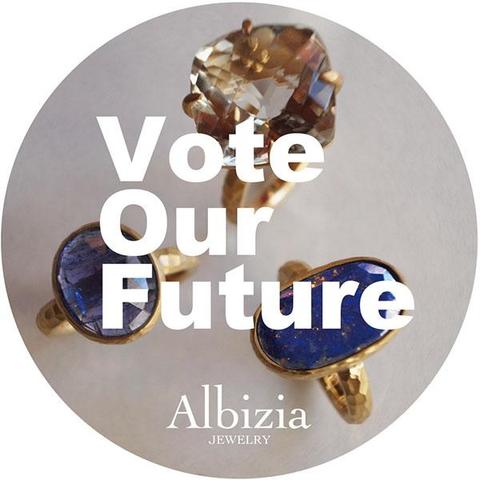 Vote Our Futureのステッカー画像です。グレーの背景に三つのリングが並び、Vote Oure Futureの文字とブランドロゴが並んでいます。丸型です。