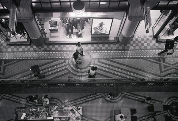 A grainy B&W photo of several people walking through the Queen Victoria Building in Sydney. The shot is very close to straight down, and the people are walking by a fashion store display window.