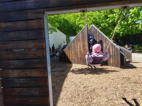 Dziecko na huśtawce na tle dziwacznej konstrukcji która jest zjezdzalniami