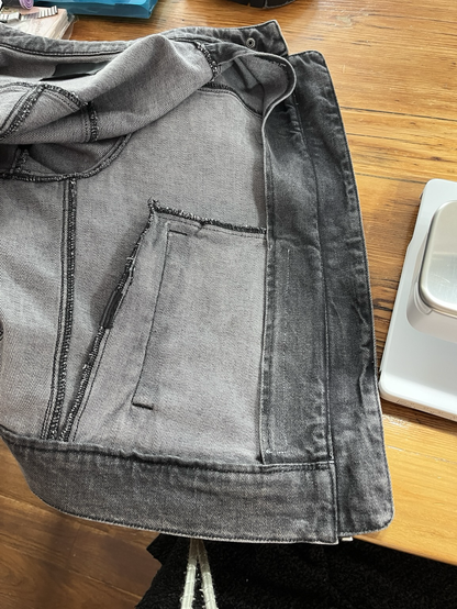 Photo présentant l'interieur d'une veste en jean grise. La poche est fermée par un scratch (non visible). Le dessus de la poche reste ouvert et accessible