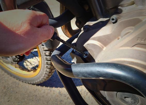 on a motorbike engine a hand is sticking the oil level checker in it