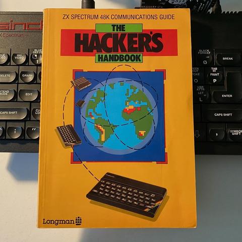 Photograph of the from cover of “The Hacker’s Handbook” a ZX Spectrum 48K communications guide by Longman publishing. The illustration depicts orbital ZX Spectrums encircling the globe.