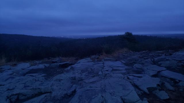 Rocky outcrops in the foreground, with hills in the distance and a cloudy sky.