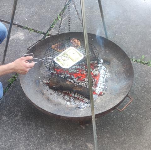 Über der Glut in einer Feuerschale, wird Essen das auf einen Grillrost liegt, der an einem Dreibein hängt warm gemacht.