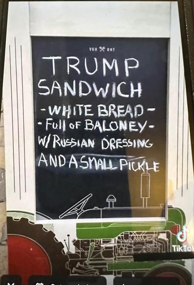 Sandwich board with this text: 
TRUMP SANDWICH:
- WHITE BREAD 
- Full oF BALONEY
- W/RWSIAN DRESSING
- AND A SMALL PICKLE