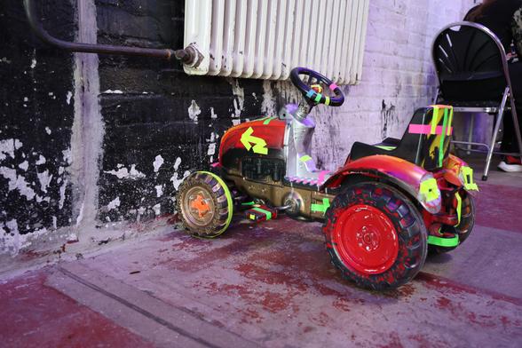 A go-cart decorated with neon tape, parking in front of a radiator.