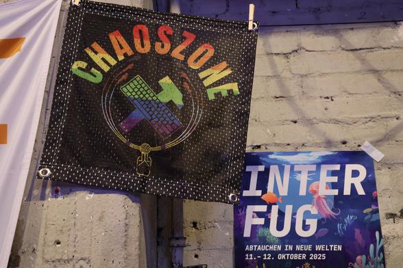Flag "Chaoszone" and poster "Inferfug 11. - 12. Oktober 2025" hanging on a wall.