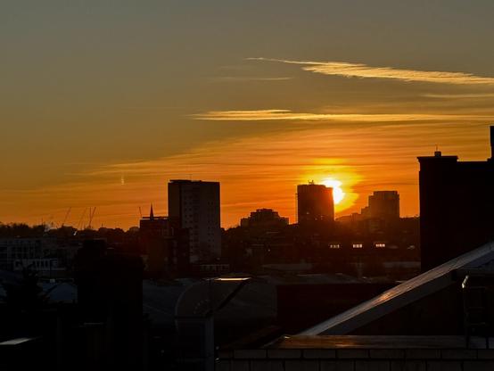 Sun setting behind a North London cityscape, in an orange sky.