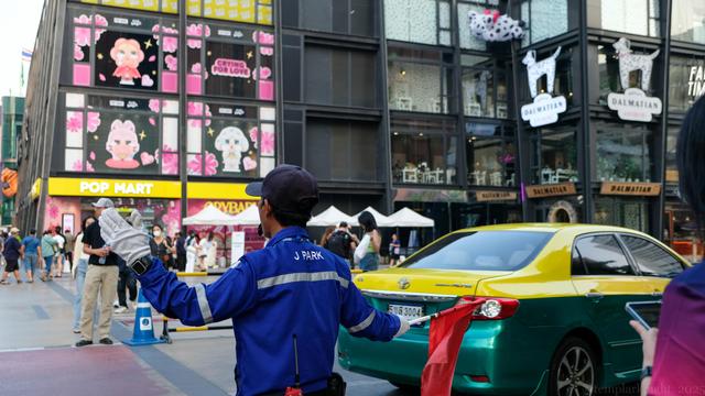 color photo of a busy shopping district in Bangkok where a parking/traffic attendant directs traffic at a street intersection