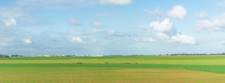 The image shows a vast, open landscape with green fields under a blue sky with scattered clouds. It's a serene rural scene, possibly of farmland or pasture.