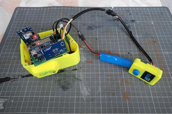 Testweiser Zusammenbau: Links liegt das offene Gehäuse des Sensors, die Elektronik ist nur oben draufgelegt. Auf der links Seite sind ein paar Kabel, eines davon geht über eine Steckverbindung zum danebenliegenden Rundzellenakku. Ebenso das Displaykabel kommt von dieser Seite und führt über einen Bogen zum Prototyp des neuen Displaygehäuses, das rechts neben dem Akku liegt. Das Display ist beleuchtet, man kann das Logo "OpenBikeSensor" sehen.