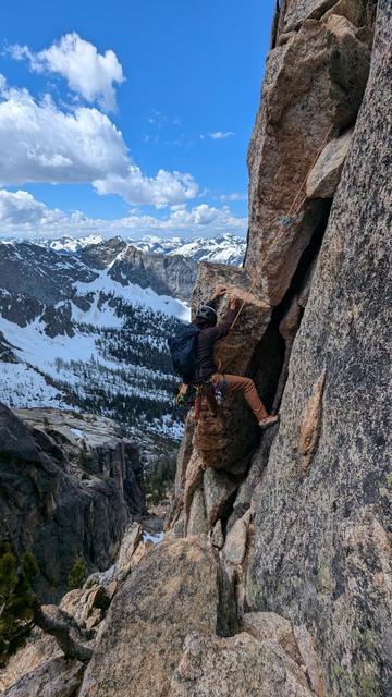 A person rock climbing. The person is attempting to transition from the inside of a crack feature, onto an awkward face.