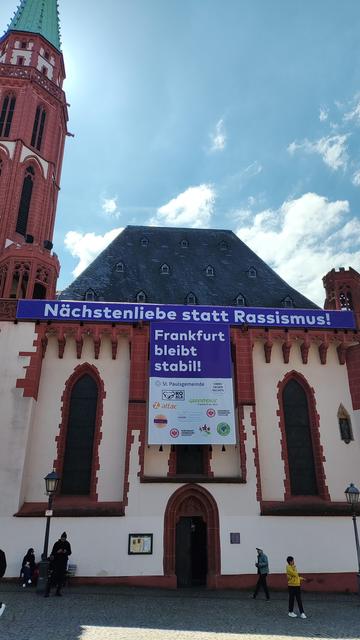 Kirche an der ein Banner hängt mit den Worten "Nächstenliebe statt Rassismus! Frankfurt bleibt stabil! 
Darunter die Logos der Paulsgemeinde, Omas gegen Rechts, Greenpeace, Koalakollektiv, Attac Eco in Good Eintracht Frankfurt Fridays for Future usw.