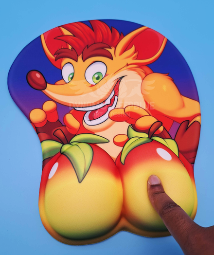 A photograph of a 3D mousepad with artwork depicting Crash Bandicoot looking excitedly at a pair of wumpa fruits that make up the raised rounded parts of the mousepad. A finger is pressing down on one of the fruits. Art and item by Dynamo-Deepblue.