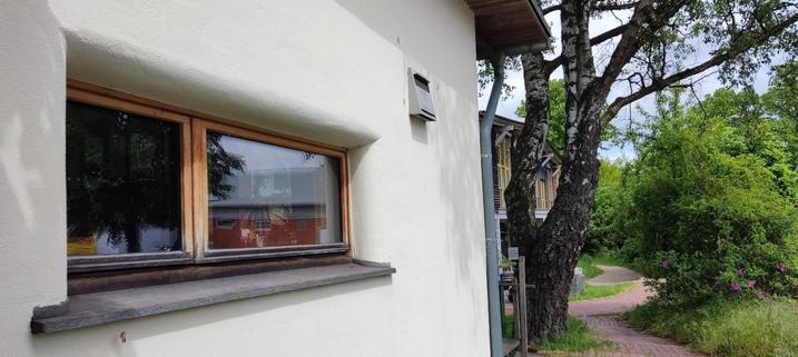 lime plasteredstraw house office building with rounded window reveals and untreated partially wethered oak boards, air in-/outlet, greenery in the background