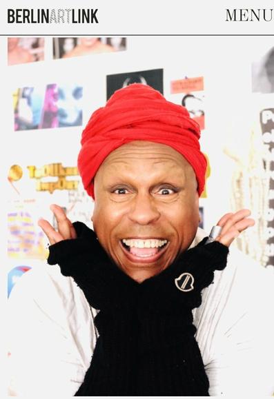 Photograph of Vaginal David by Ryan Molnar, wearing white dress by Oak with black arm warmers by Rick Owens/ Moncler and red turban by Louisa Brandt.