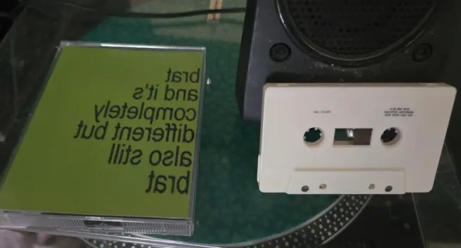 A white cassette sitting next to the double tape case for the brat remix album