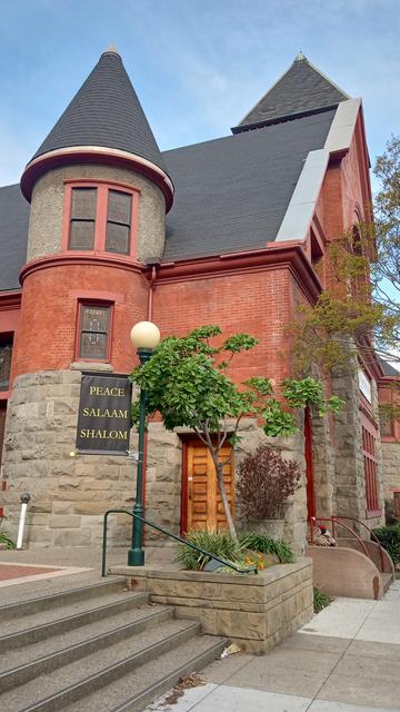 A big brick Romanesque Church. A banner in front says peace/salaam/shalom.