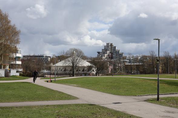 A photo of buildings and grass on a sunny spring day. There is a cyclist on a road.
