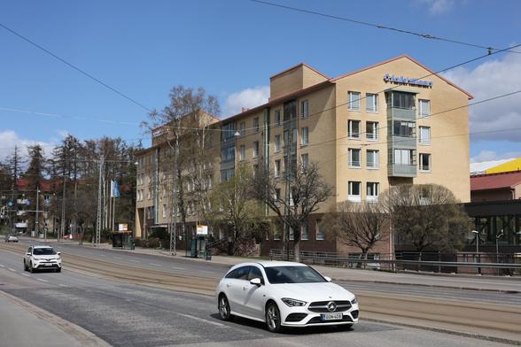 A photo of Mannerheimintie in Helsinki on a sunny spring day. There is a white car in the foreground.