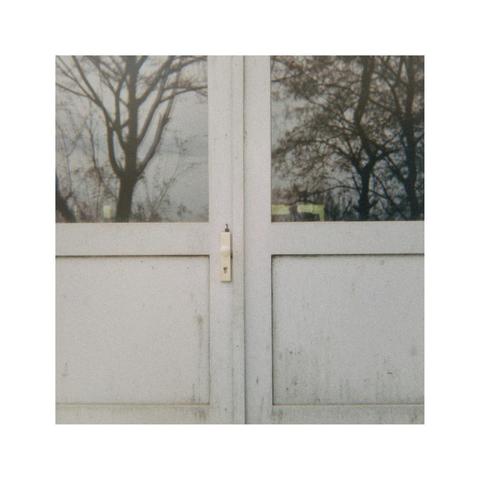 a square picture of an old wooden glass door. the windows are reflecting the sky and some still leafless trees
