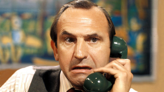 Image shows Leonard Rossiter as the character Reggie Perrin. He is engaged in a telephone call