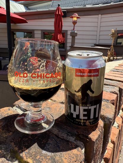 A snifter glass half full of dark beer next to a silver can with a Yeti in silhouette